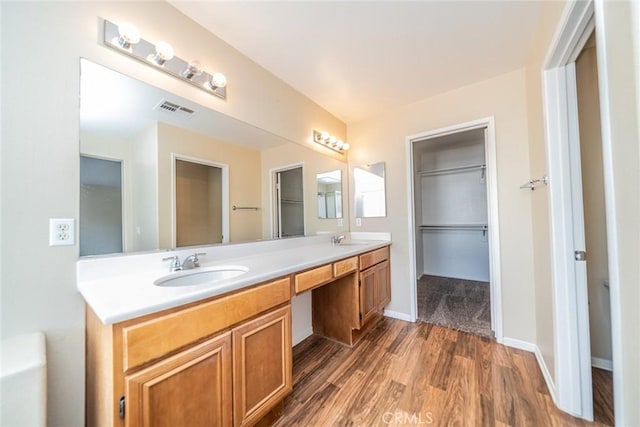 full bath with double vanity, visible vents, a sink, and wood finished floors