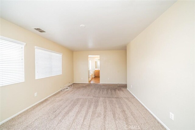 unfurnished room with visible vents, light colored carpet, and baseboards