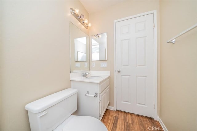 half bath with toilet, wood finished floors, vanity, and baseboards