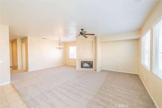 unfurnished living room featuring ceiling fan with notable chandelier, light colored carpet, a tiled fireplace, and baseboards