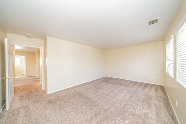 empty room featuring visible vents, light colored carpet, and baseboards