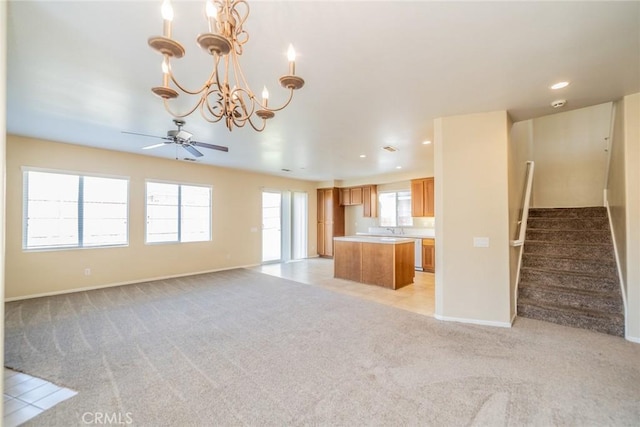 unfurnished living room featuring light carpet, recessed lighting, stairway, ceiling fan with notable chandelier, and a sink
