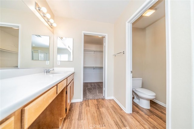 bathroom with toilet, a walk in closet, vanity, and wood finished floors