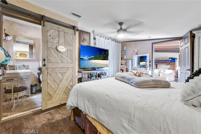 bedroom with a barn door, visible vents, a ceiling fan, and wood finished floors