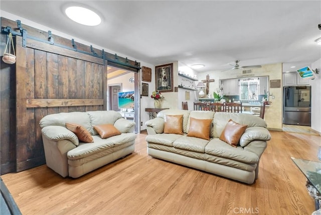 living area with ceiling fan, a barn door, and light wood-style floors