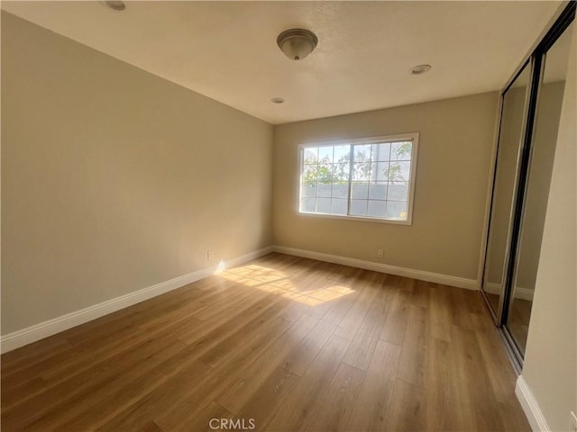 unfurnished bedroom with wood finished floors, baseboards, and a closet