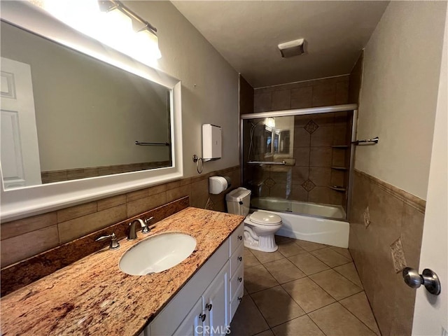 bathroom featuring shower / bath combination with glass door, vanity, tile patterned flooring, toilet, and tile walls