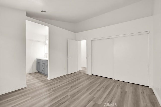 unfurnished bedroom featuring light wood-type flooring, baseboards, a sink, and a closet