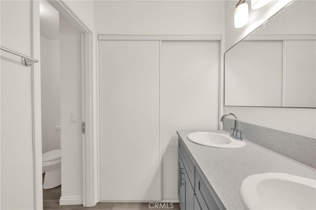 full bath with double vanity, toilet, wood finished floors, and a sink