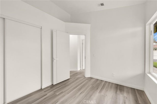 unfurnished bedroom with baseboards, light wood finished floors, visible vents, and a closet