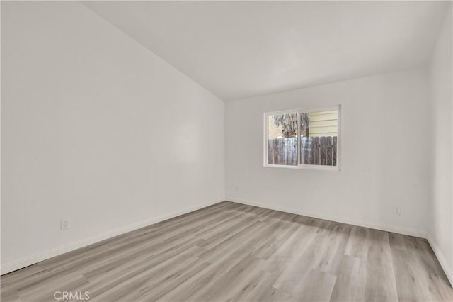 spare room featuring light wood finished floors, vaulted ceiling, and baseboards