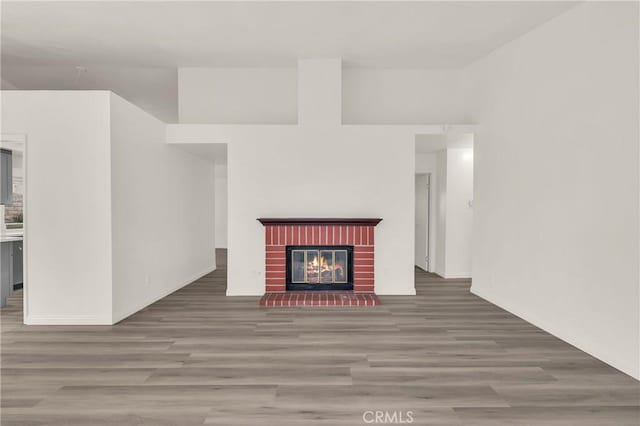 unfurnished living room with baseboards, a brick fireplace, and wood finished floors