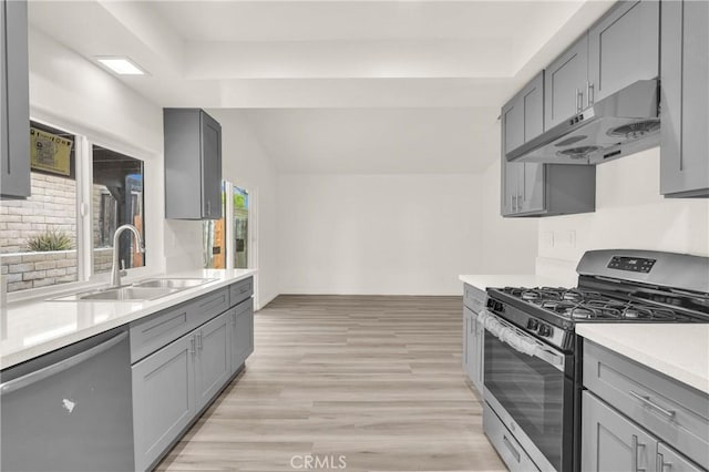 kitchen with under cabinet range hood, gray cabinets, appliances with stainless steel finishes, and a sink