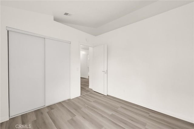 unfurnished bedroom featuring wood finished floors, a closet, and visible vents