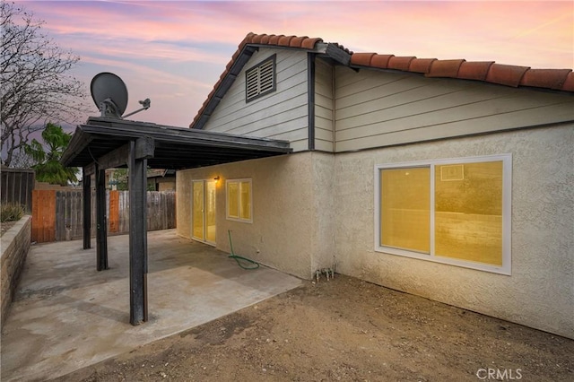 back of house at dusk with fence, a patio area, a tile roof, and stucco siding