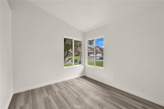 unfurnished room with baseboards, vaulted ceiling, and wood finished floors
