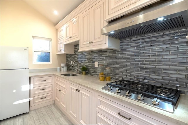 kitchen with freestanding refrigerator, exhaust hood, stainless steel gas cooktop, lofted ceiling, and a sink