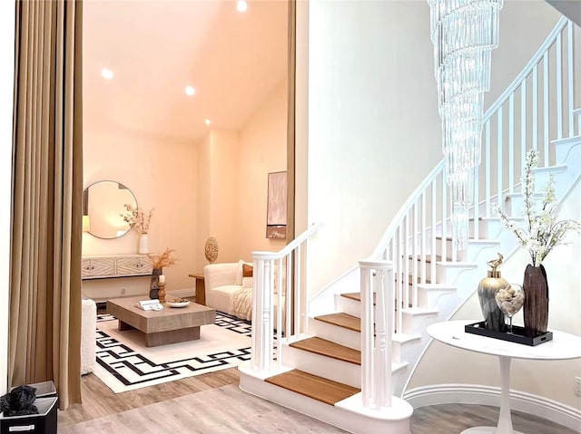 staircase with high vaulted ceiling, a notable chandelier, and wood finished floors