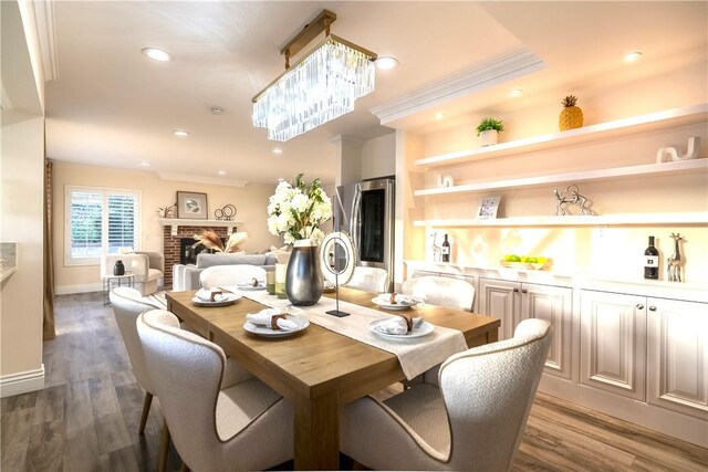 dining space with a brick fireplace, dark wood-style flooring, a chandelier, crown molding, and recessed lighting