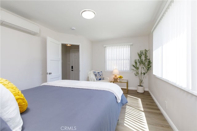 bedroom featuring a wall mounted AC, light wood finished floors, and baseboards