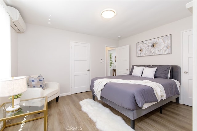 bedroom with light wood-style floors, baseboards, and an AC wall unit