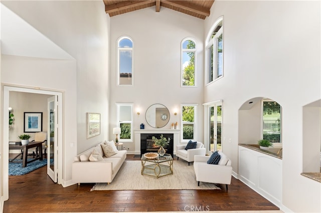 living area with high vaulted ceiling, beamed ceiling, a wealth of natural light, and dark wood-style flooring