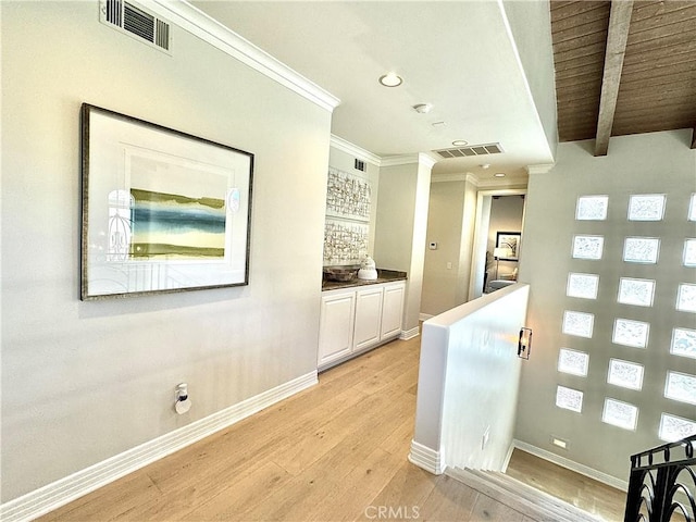 corridor featuring crown molding, visible vents, light wood-style flooring, and baseboards