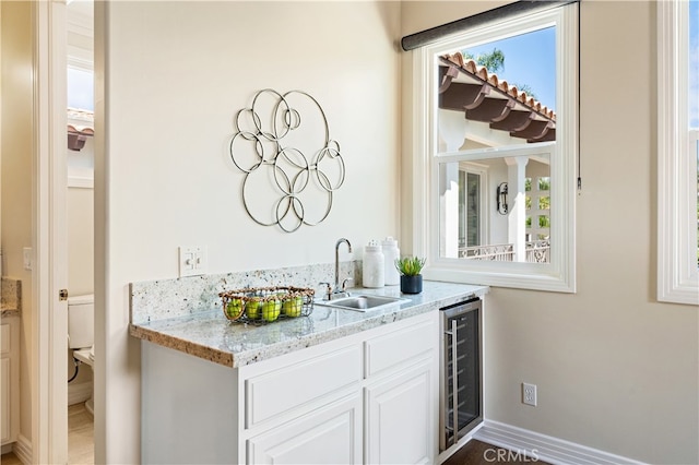 bar with a sink, baseboards, beverage cooler, and indoor wet bar
