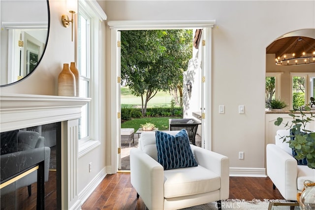 sitting room featuring arched walkways, a fireplace, dark wood-style floors, and baseboards