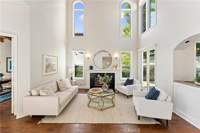 living area with a glass covered fireplace, arched walkways, wood-type flooring, and a towering ceiling