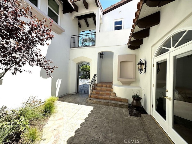 view of exterior entry featuring french doors, a tile roof, stucco siding, and a balcony