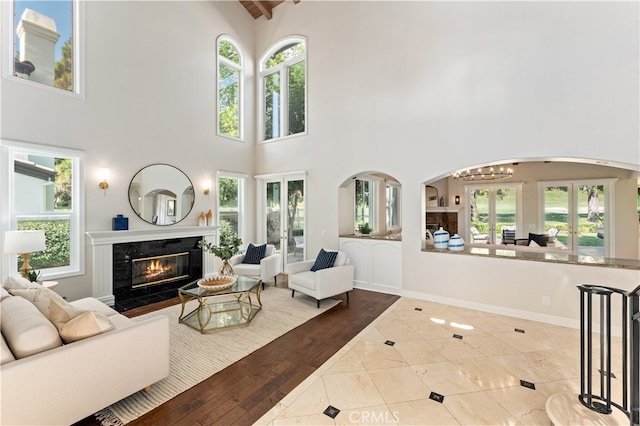 tiled living area featuring arched walkways, a high end fireplace, a high ceiling, and a healthy amount of sunlight
