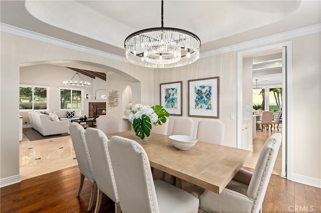 dining room with baseboards, arched walkways, a chandelier, crown molding, and a tray ceiling