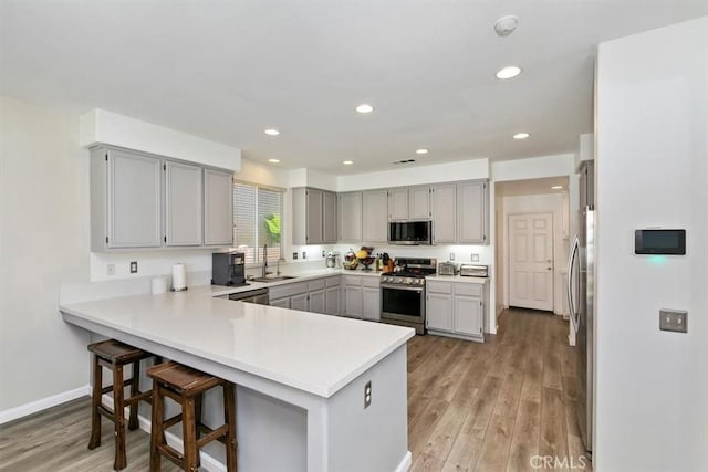 kitchen with gray cabinets, a peninsula, light wood-style flooring, stainless steel appliances, and a sink
