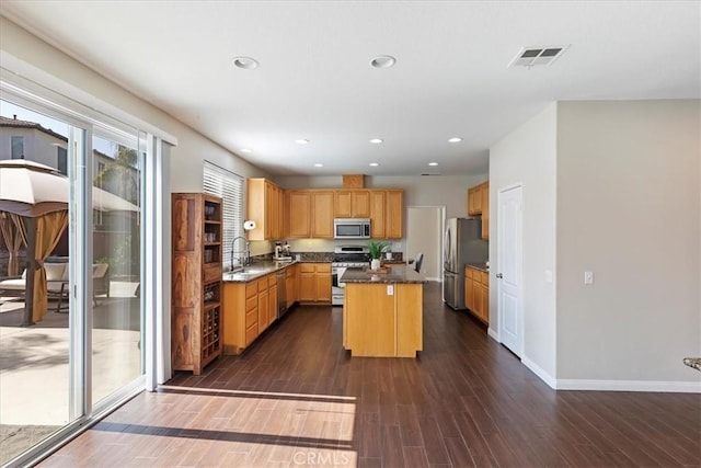 kitchen with visible vents, a kitchen island, a sink, stainless steel appliances, and dark wood-style floors