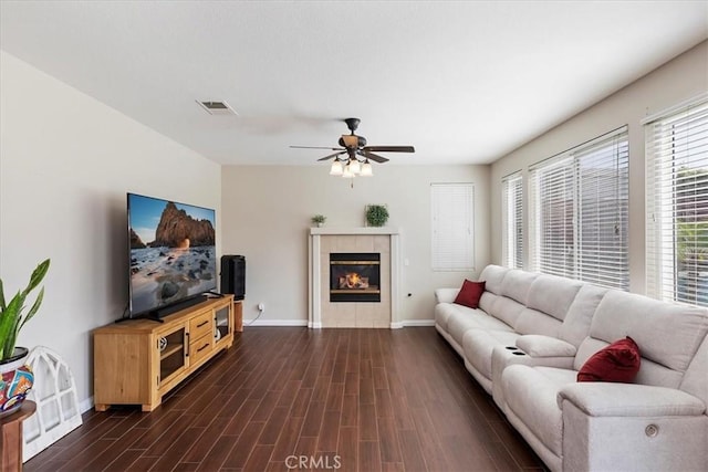 living room with a fireplace, dark wood-type flooring, a ceiling fan, visible vents, and baseboards
