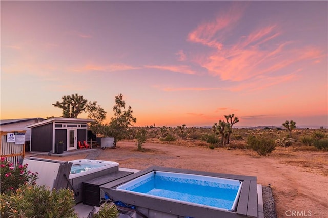 pool at dusk featuring an outdoor structure and hot tub deck surround