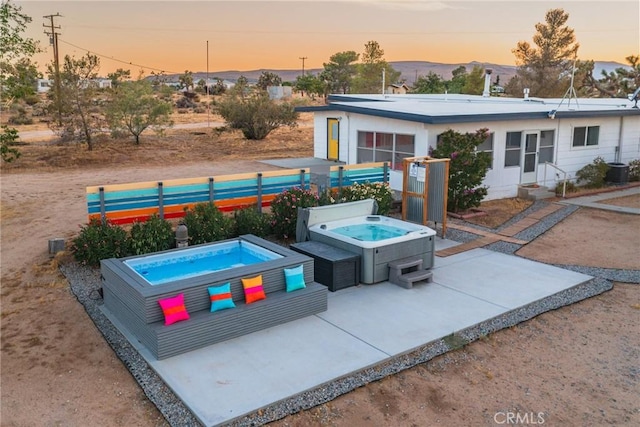 back of property at dusk featuring a patio, a mountain view, entry steps, a hot tub, and fence