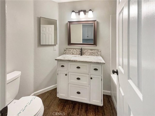 bathroom with toilet, vanity, wood finished floors, and baseboards