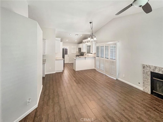 unfurnished living room with ceiling fan with notable chandelier, a fireplace, dark wood-type flooring, lofted ceiling, and baseboards