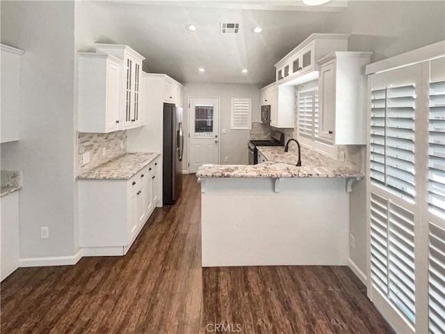 kitchen featuring visible vents, glass insert cabinets, a peninsula, light stone countertops, and stainless steel appliances