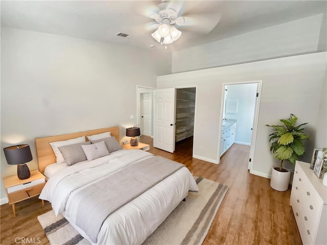 bedroom featuring baseboards, visible vents, wood finished floors, a high ceiling, and a walk in closet