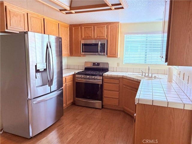 1244 Winged Foot Dr, Upland, CA 91786 - kitchen with stainless steel appliances, tile counters, a sink, light wood-type flooring, and a textured ceiling