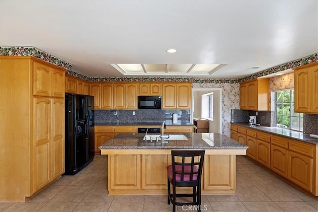 kitchen featuring a sink, light tile patterned floors, black appliances, and an island with sink