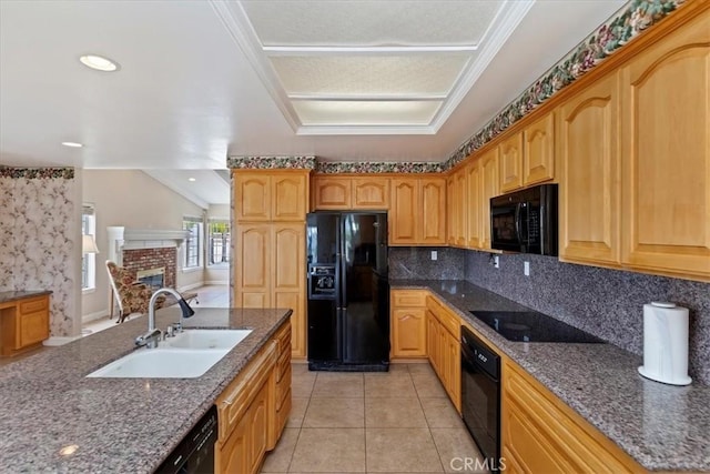 kitchen with black appliances, a brick fireplace, dark stone counters, decorative backsplash, and a sink