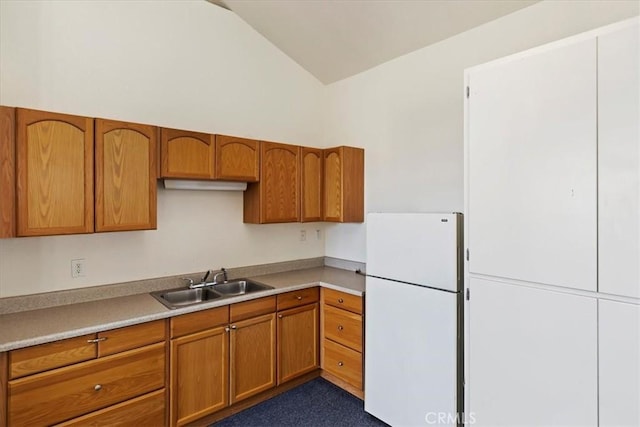 kitchen with vaulted ceiling, light countertops, freestanding refrigerator, brown cabinets, and a sink