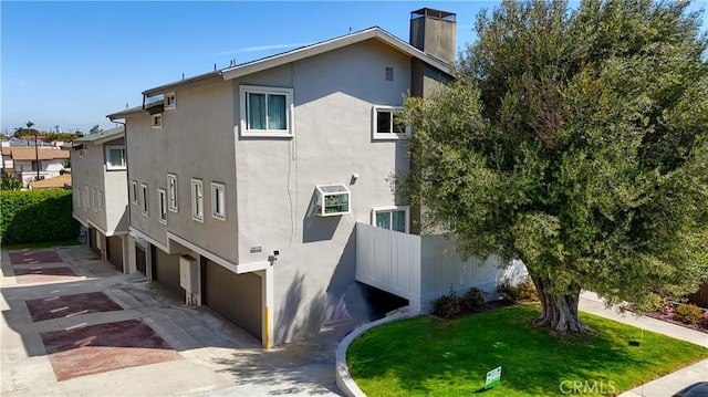 view of side of property featuring a yard, a garage, a chimney, concrete driveway, and stucco siding