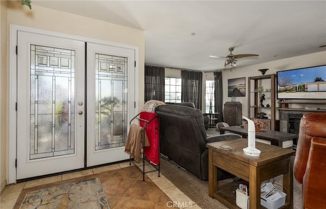 tiled living room with french doors, a ceiling fan, and a glass covered fireplace