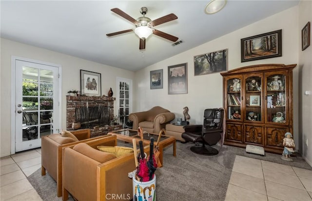 living area featuring lofted ceiling, light tile patterned floors, a brick fireplace, visible vents, and ceiling fan