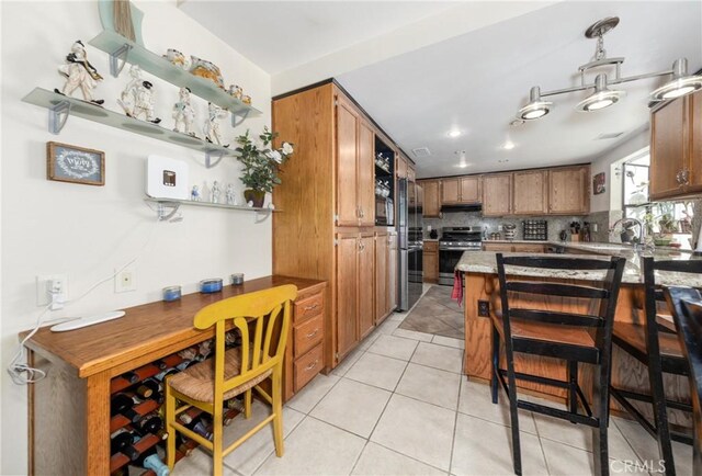 kitchen with tasteful backsplash, light countertops, stainless steel stove, brown cabinets, and light tile patterned flooring